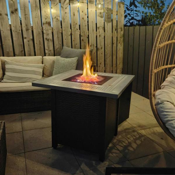 Black and grey gas firepit table with flames on top in outdoor seating area