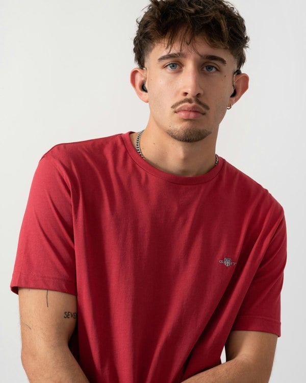 Man wearing a red t-shirt with a brand logo on a white background