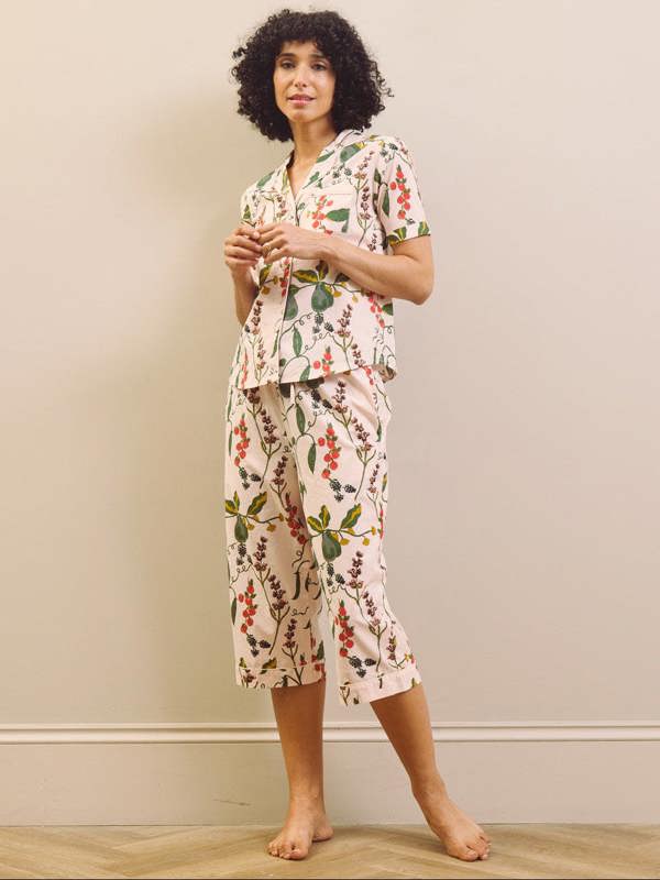 Woman wearing a pear & floral capri pyjama set against a plain wall.