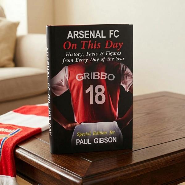 Personalised Arsenal FC On This Day book displayed upright on a wooden coffee table next to a red and white scarf.