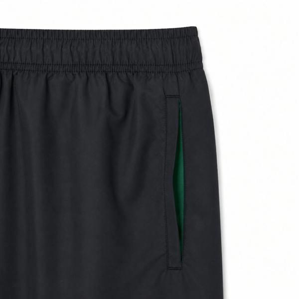Lacoste black quick-dry swim shorts featuring an elastic waistband and a green-lined side pocket.