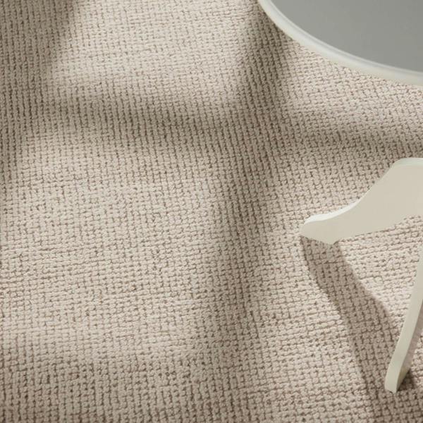 Textured beige fabric with a small white decorative item on a neutral background