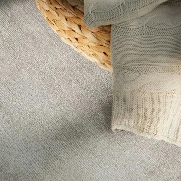 Light gray textured fabric with a woven basket and beige knitted blanket on a light gray surface.