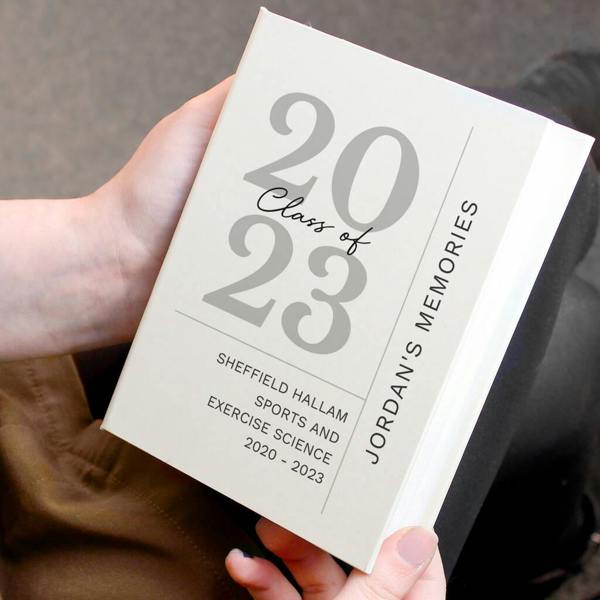 A person holding a personalised cream graduation photo album printed with Class of 2023, Sheffield Hallam University details, and a vertical name text line.