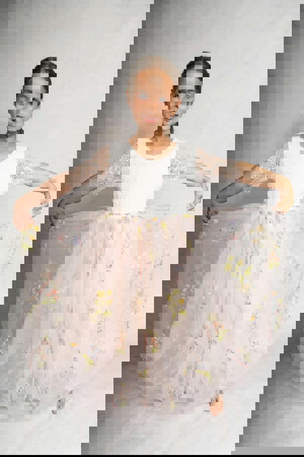 Young girl wearing a white dress with floral embroidery on a plain background