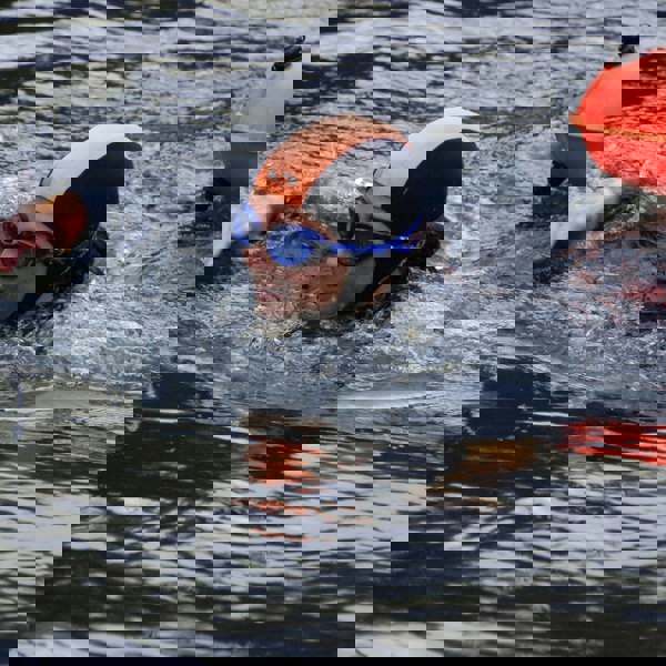 Person swimming in water with a swim cap and goggles, accompanied by an inflatable tube.