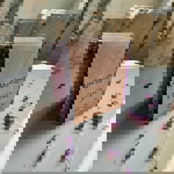 Lavender soap bar with a brown paper label on a stone surface with lavender flowers.