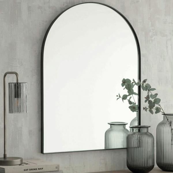 Black arched wall mirror styled on a console table in a modern hallway.