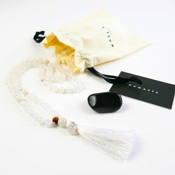 Kati Kaia crystal moonstone mala necklace with white beads and tassel next to cream pouch and black stone