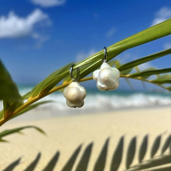 Flower-shaped pearl earrings displayed on an exotic Caribbean beach by LENAE London.