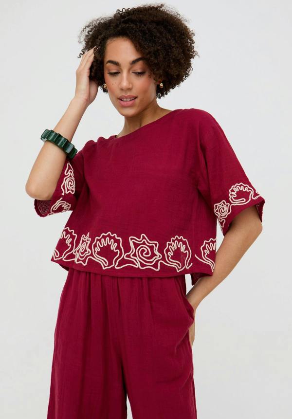 Woman wearing a burgundy outfit with white floral patterns on a plain background