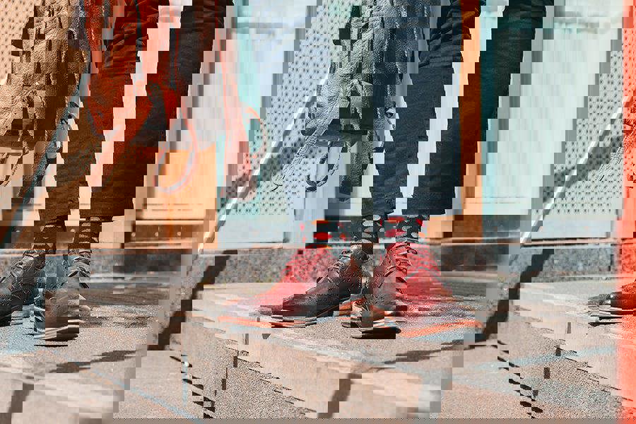 Person wearing brown leather shoes and spotty socks standing on a step with a backpack in the background.