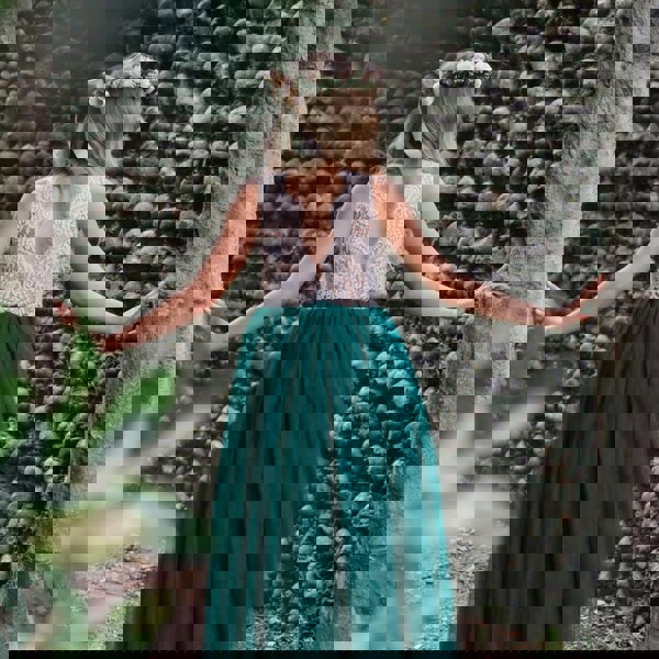 Girl in a green dress with a floral headband standing against a textured stone wall.