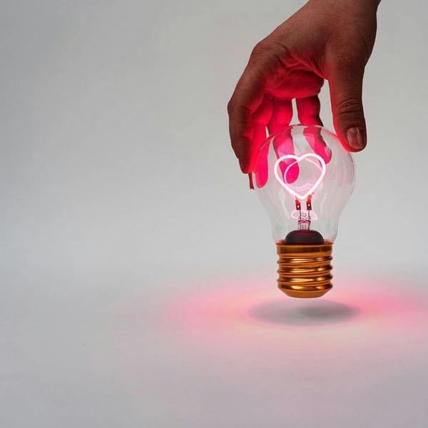 Hand holding a cordless Edison lightbulb showing an illuminated pink LED heart filament.