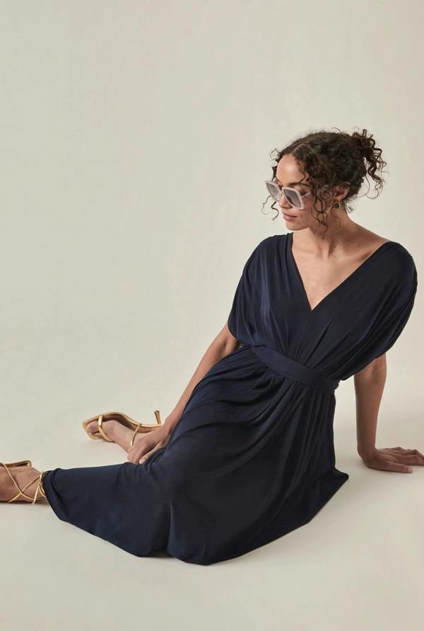 Model wearing the Draped Open-Back Midi Dress in Navy by James Lakeland for an elegant occasion look sitting down on the beige background
