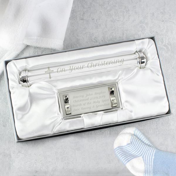 A personalised silver-plated christening certificate holder and custom engraved base beautifully presented inside a silk-lined gift box, styled with a soft white baby blanket and blue striped knitted sock.