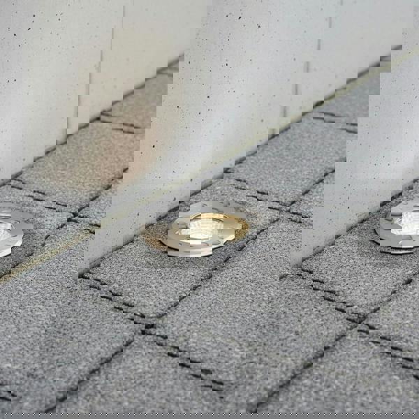 stainless steel outdoor ground lamp mounted in the ground next to a wall 