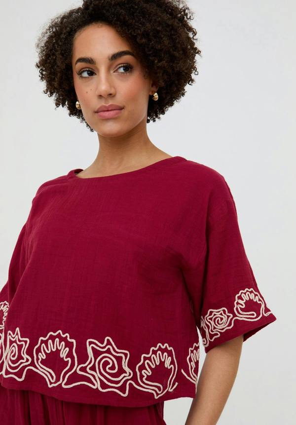 Woman wearing a burgundy top with white floral patterns on a plain background