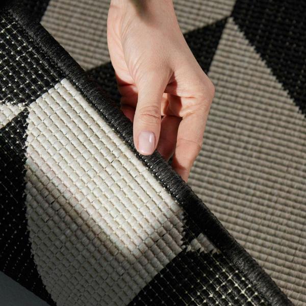 Hand holding a corner of a black and white patterned rug