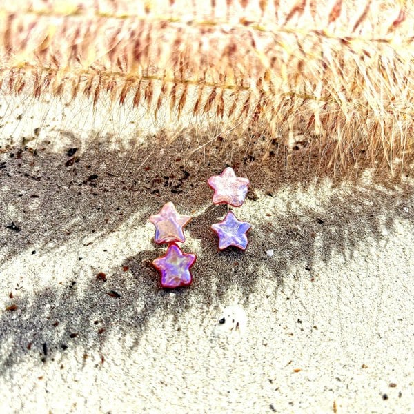 Pink star-shaped pearl ear jacket earrings by LENAE on sandy beach.