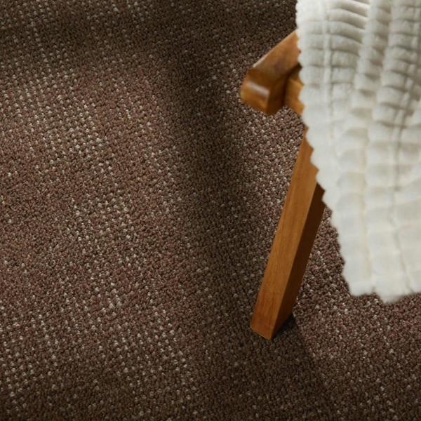Brown textured carpet with a wooden chair leg and white fabric edge.