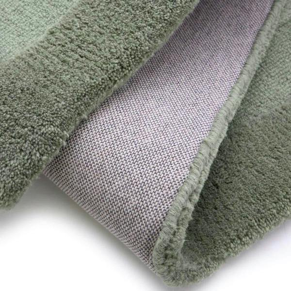 Close-up of a green textured rug with a gray woven pattern underneath on a white background.
