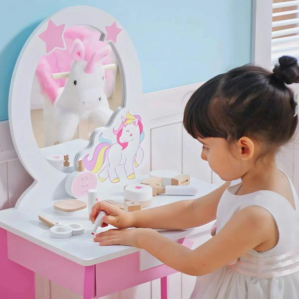 Young child applying makeup at pink kids dressing table with unicorn mirror
