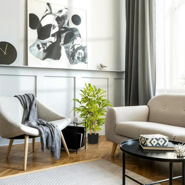 Artificial bamboo tree in black pot on floor beside a sofa in a living room setting