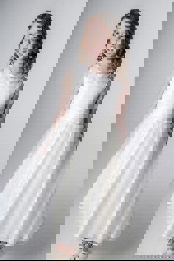 Young girl wearing a ivory dress against a plain background