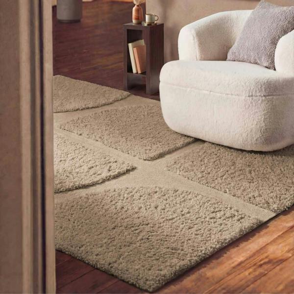 Beige area rug on a wooden floor with a white armchair in the corner.