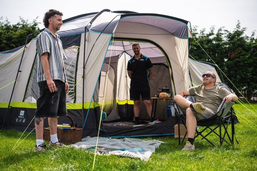 A group of males relaxing outside of the Hive 6 Berth Poled Tent by OLPRO