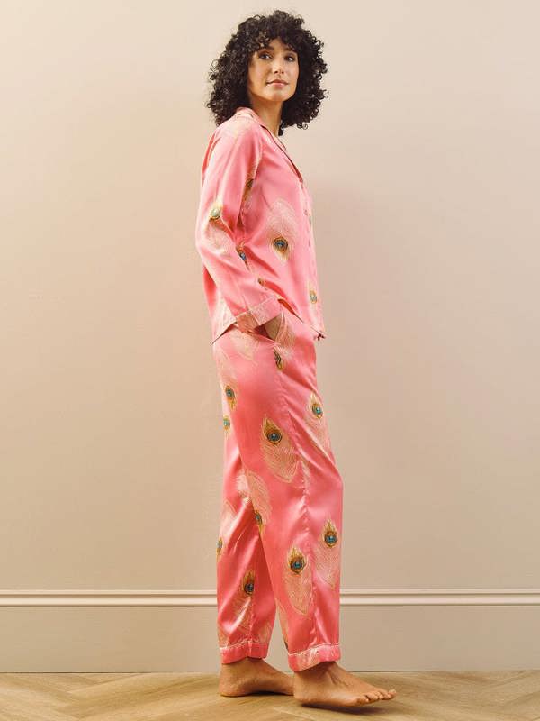 Person wearing pink pyjamas with a peacock feather pattern in a room with a beige wall and wooden floor.