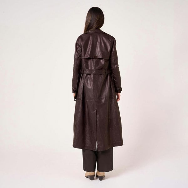 Image shows a model facing away from camera. She wears a long burgundy trench coat made from real leather. The hem of the coat lands mid-calf.