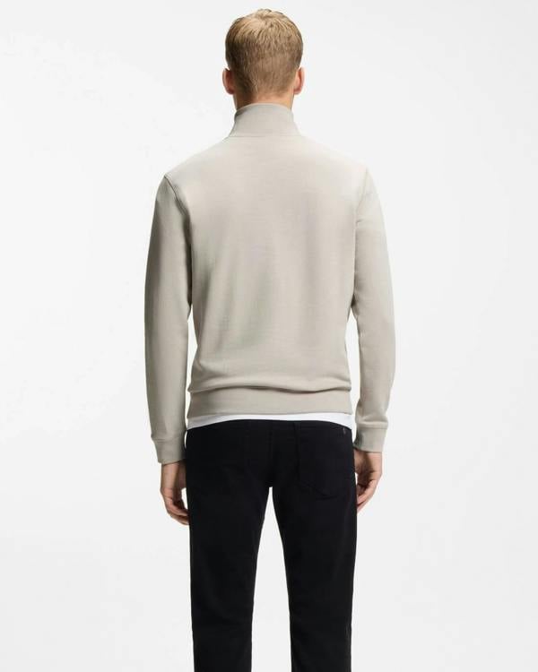 Man wearing a light gray sweater and dark pants on a white background