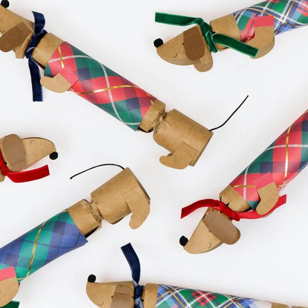 Close-up view of sausage dog Christmas crackers showing tartan paper coats, velvet scarves, pompom noses, and gold foil accents.