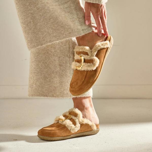 Brown slippers with fur trim worn by a person in a beige sweater.
