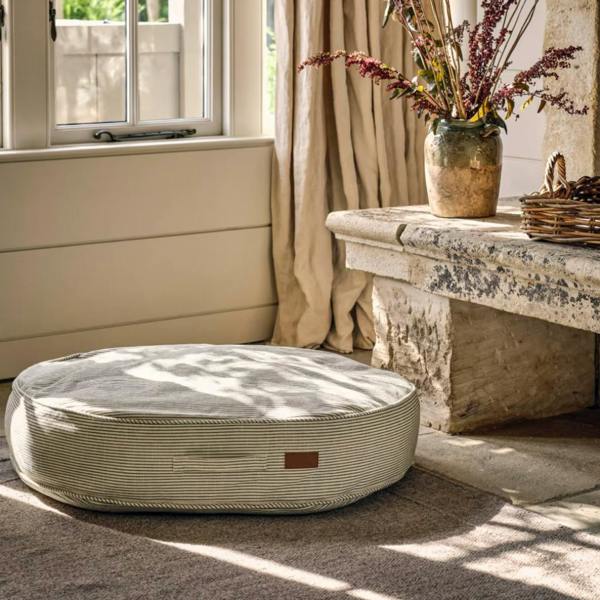Large sage green and cream ticking stripe oval dog cushion on a neutral rug.