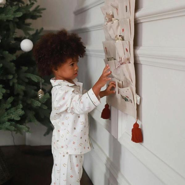 A young child wearing white and green Nutcracker print organic cotton flannel pyjamas, reaching into a fabric hanging pocket advent calendar.