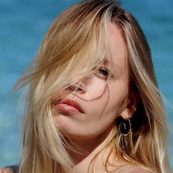 A blonde model with hai all over face wearing spiral gold vermeil hoops.