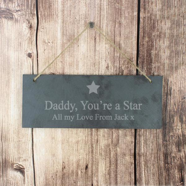 A personalised hanging slate plaque with an engraved star motif by Abode Home & Gifts, featuring the bold message "Daddy you're A Star" and "All my Love from Jack x" on a rustic stone texture, shown hanging against a wooden wall.