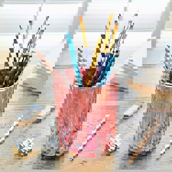 A multicoloured vase filled with pens and pencils on a table.