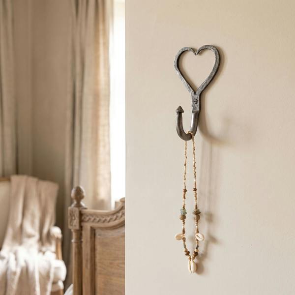 Small cast iron heart-shaped coat hook mounted on a painted wall in a vintage shabby-chic bedroom.