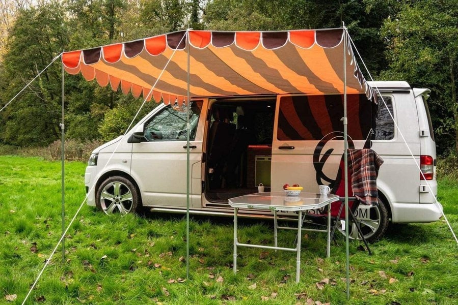 An image of the OLPRO Orange and Brown Campervan Canopy on the VW T5 Campervan in a field with a treeline in the background.