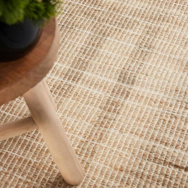 Close-up of a textured beige rug with a wooden stool and plant in the corner.