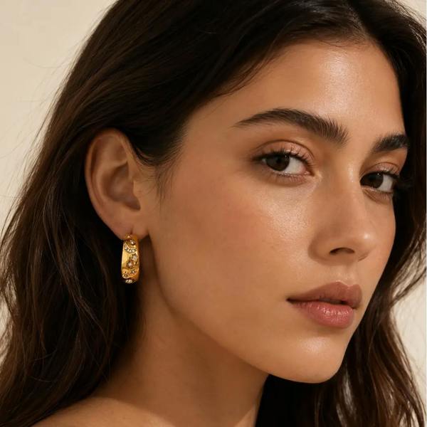 Close-up of a woman wearing gold hoop earrings with a neutral background