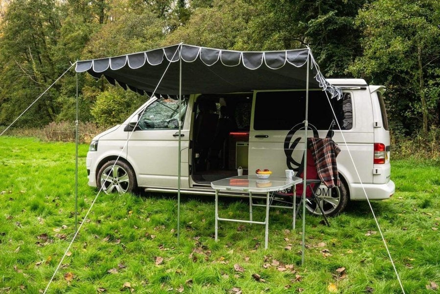 An image of the OLPRO Charcoal Campervan Canopy on the VW T5 Campervan in a field with a treeline in the background.