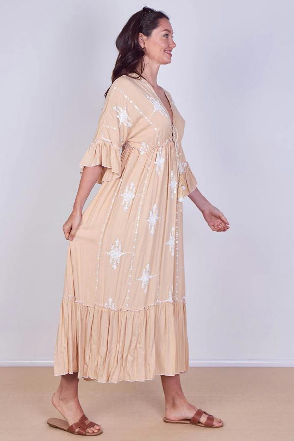 Woman wearing a beige dress with white floral patterns on a plain background