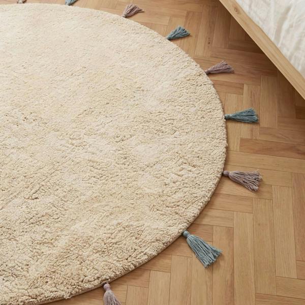 Round beige rug with tassels on a wooden floor