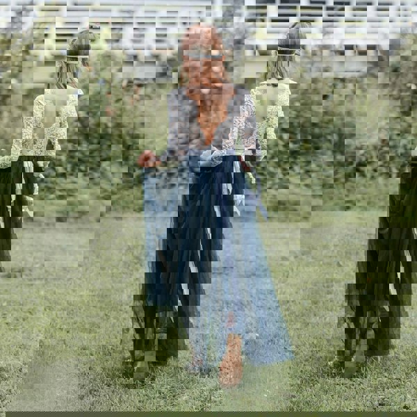 Girl in a lace top and navy blue skirt standing in a grassy field.