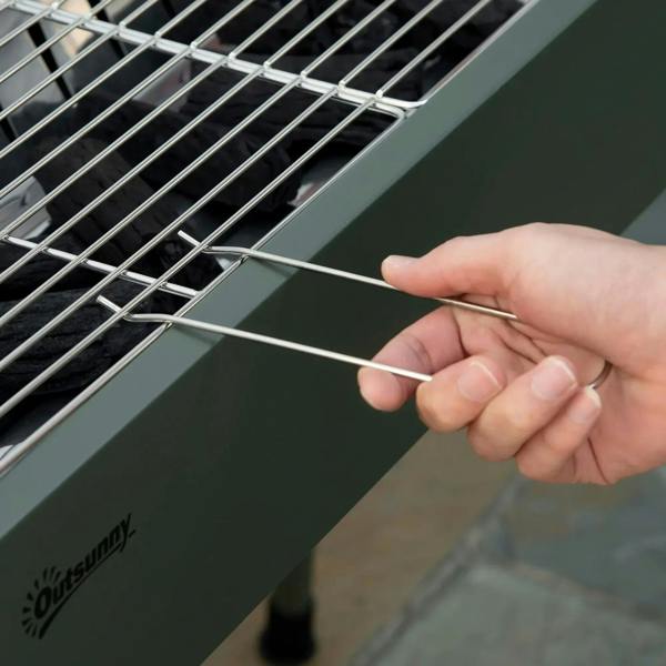 Green charcoal BBQ grill cooking grate with hand using tong to lift a wire section